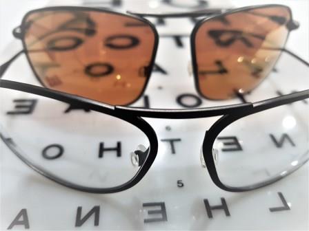 Clear and tinted prescription sunglasses sitting on an opticians eye test chart