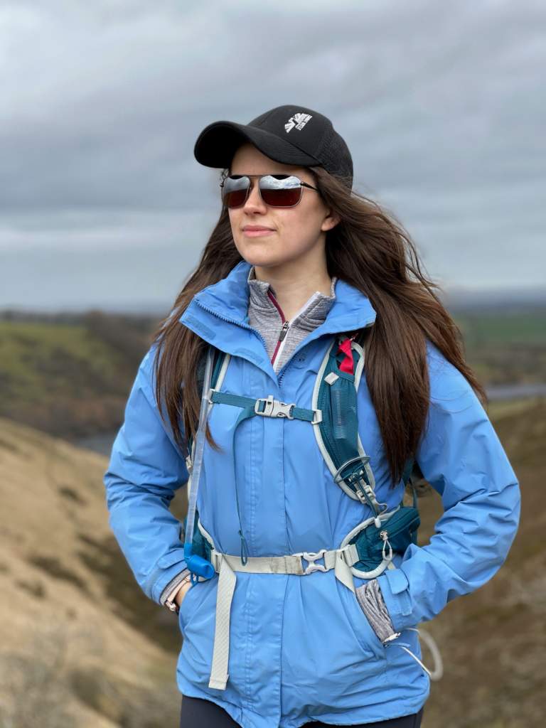 Young woman hiking in dartmoor wearing blue jacket baseball cap and Bigatmo sunglasses